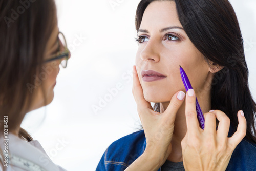 Plastic surgeon drawing dashed lines on her patient s face.