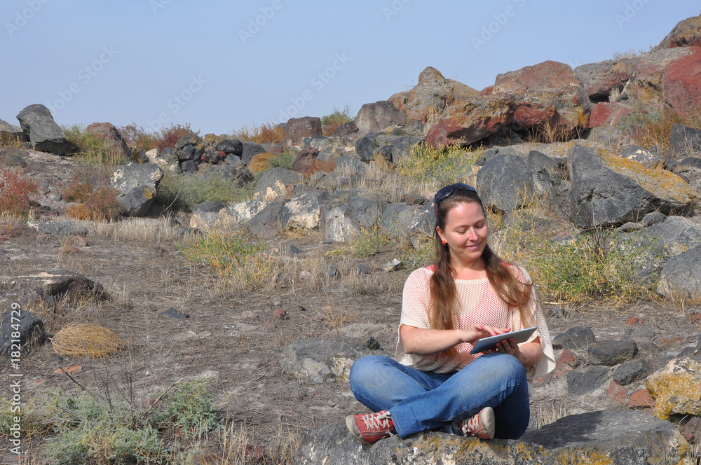 Young woman sitting among gray stones and working on a tablet computer