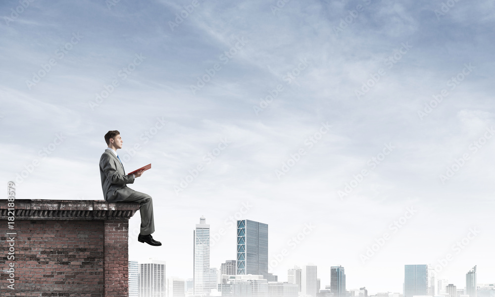 Man on roof edge reading book and cityscape at background Man on roof edge reading book and cityscape at background