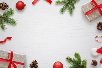 White table with Christmas decorations and space in the middle for text. Christmas composition with gifts, fir branches, lollipop, Santa hat and pinecones. Top view.