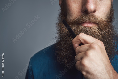 Fotobehang Handsome young man styling his beard with a comb