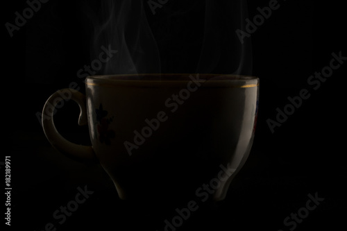 Black cup of coffee with steam on black background.