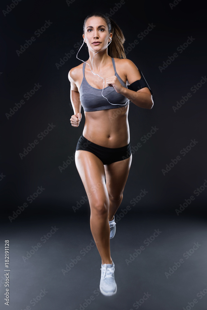 Fit and sporty young woman running over black background.
