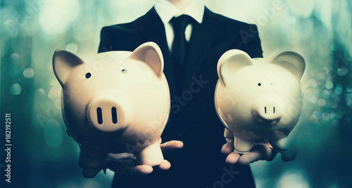 Businessman holding two piggy banks on blue abstract light background