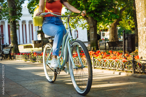 Closeup of young beautiful woman riding vintage bicycle in summer park. Green trees background
