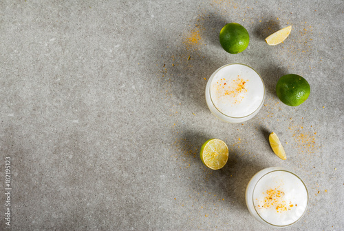 Peruvian, Mexican, Chilean traditional drink pisco sour liqueur, with fresh lime, on gray stone table, copy space top view