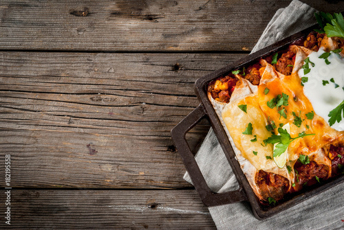 Mexican food. Cuisine of South America. Traditional dish of spicy beef enchiladas with corn, beans, tomato. On a baking tray, on old rustic wooden background. Top view copy space