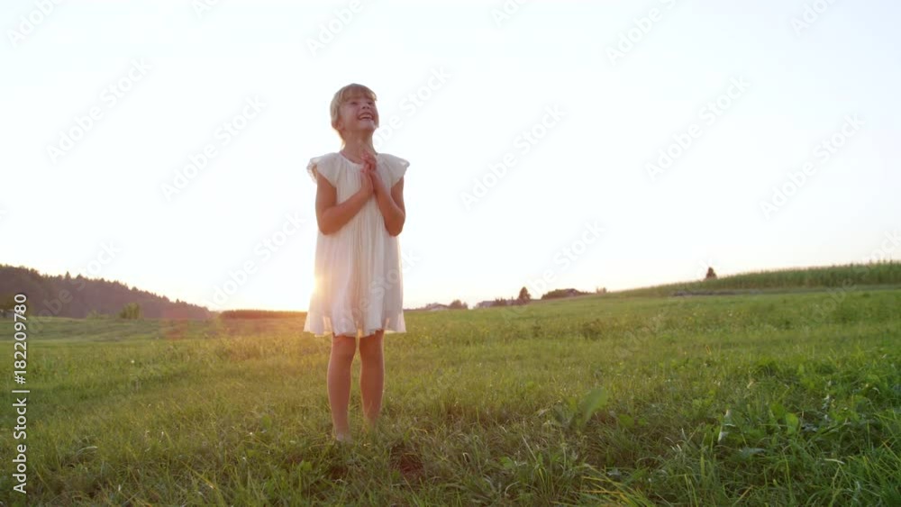 SLOW MOTION CLOSE UP Silly little girl in white dress having fun outdoors in late afternoon. Goofy child enjoying her summer playing in a meadow at sundown. Excited little sister clapping cheerfully. SLOW MOTION CLOSE UP Silly little girl in white dress having fun outdoors in late afternoon. Goofy child enjoying her summer playing in a meadow at sundown. Excited little sister clapping cheerfully.