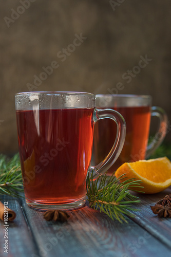 Tea in a glass mug, cinnamon stick, orange and fir branch.