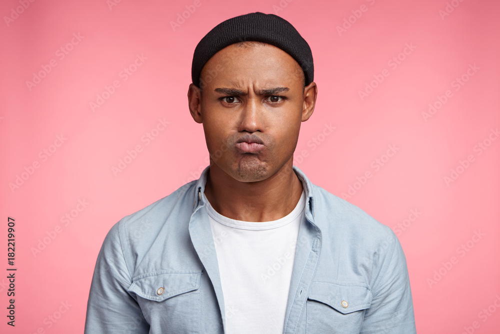 Grumpy dissatisfied mixed race male pouts lips, being angry with someone or offended, has unhappy expression, expresses his discontent. Black stylish male in fashionable clothes looks unhappy Grumpy dissatisfied mixed race male pouts lips, being angry with someone or offended, has unhappy expression, expresses his discontent. Black stylish male in fashionable clothes looks unhappy