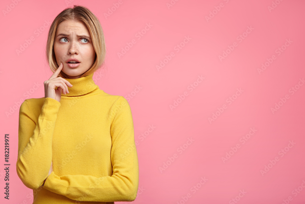 Young attractive blonde female student dressed casually, has thoughtful expression as thinks over her future actions and plans in life, going to graduate and find successful job. Copy space for text Young attractive blonde female student dressed casually, has thoughtful expression as thinks over her future actions and plans in life, going to graduate and find successful job. Copy space for text