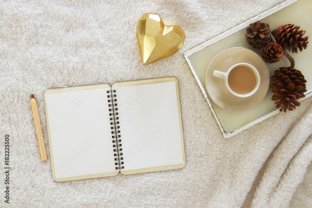 Empty notebook and cup of cappuccino over cozy and warm fur carpet. Top view.