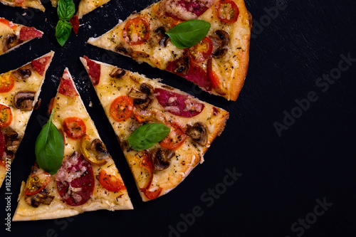 Hot and delicious pizza with salami tomatoes cheese and mushrooms ready to eat on a black wooden background. Top view.