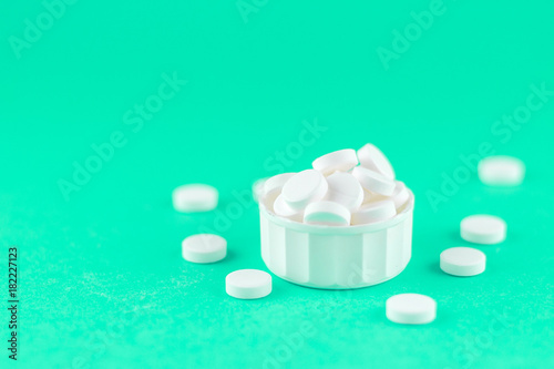 Close up white pills and capsules in cap on aquamarine background with copy space. Focus on foreground, soft bokeh. Pharmacy drugstore concept