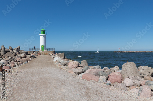 Lighthouse on the moll and a man near it, yacht in the sea