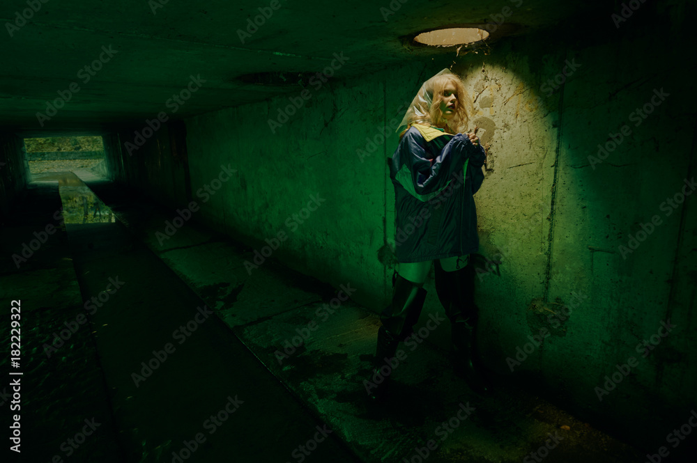 dystopian portrait of model posing in the river of sewage in tunnel under city. Lit with green light