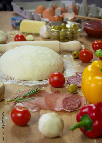 Ingredients for the preparation pizza on wooden background. Dough, tomato, olives, garlic, rosemary ...