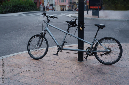 Double bike tandem is tied to the pole with a padlock.