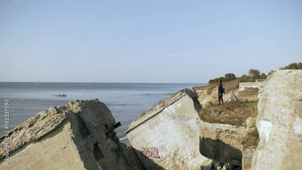 Young woman stands at collapsed fort ruins on a rock cliff in Liepaja Young woman stands at collapsed fort ruins on a rock cliff in Liepaja