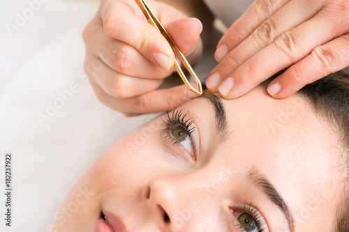 Kosmetikstudio Augenbrauen werden von Hand mit Pinzette bei junger Frau gezupft