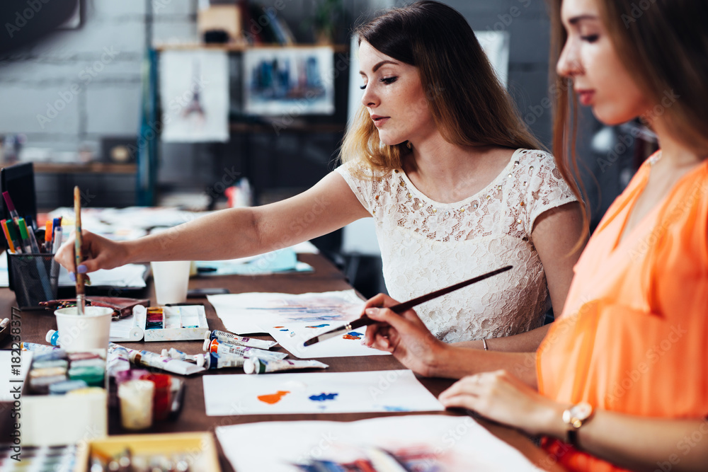 Two adult female students working on their paintings studying at art school