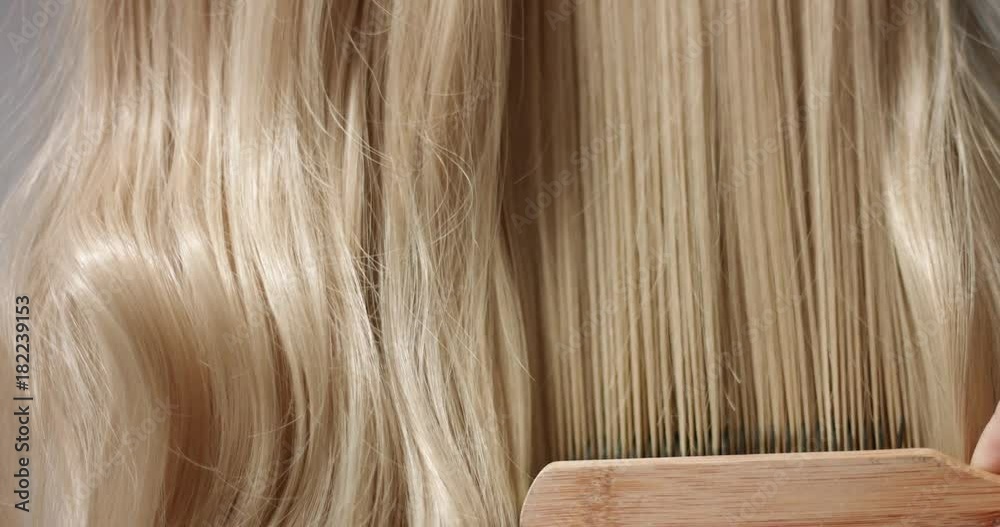 Close up shot of brushing long wavy woman's blond hair with a hairbrush Close up shot of brushing long wavy woman's blond hair with a hairbrush