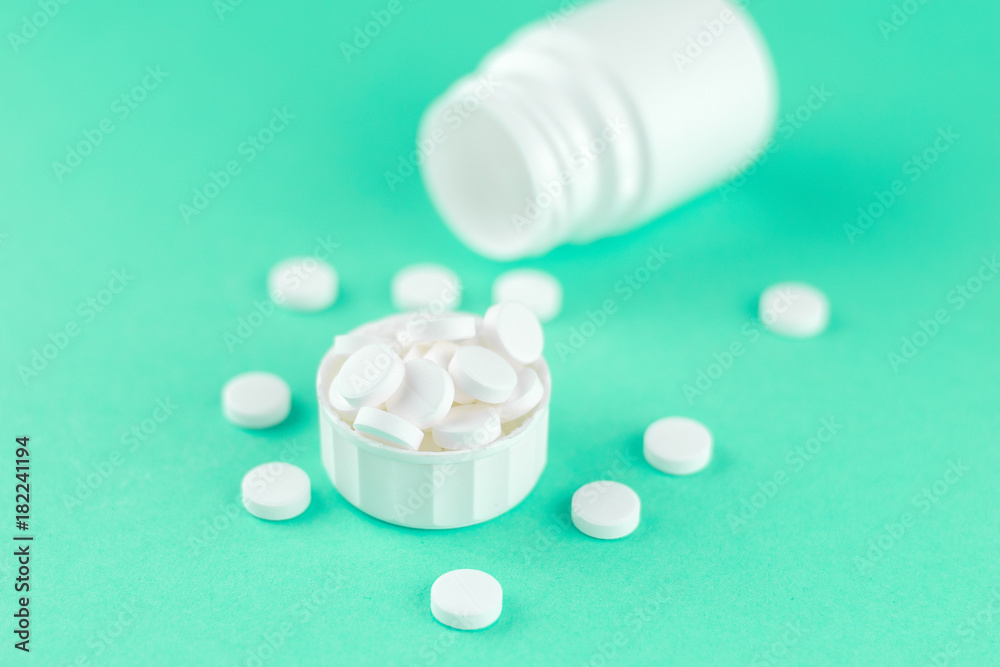 Close up white pill bottle with spilled out pills and capsules in cap on aquamarine background with copy space. Focus on foreground, soft bokeh. Pharmacy drugstore concept Close up white pill bottle with spilled out pills and capsules in cap on aquamarine background with copy space. Focus on foreground, soft bokeh. Pharmacy drugstore concept