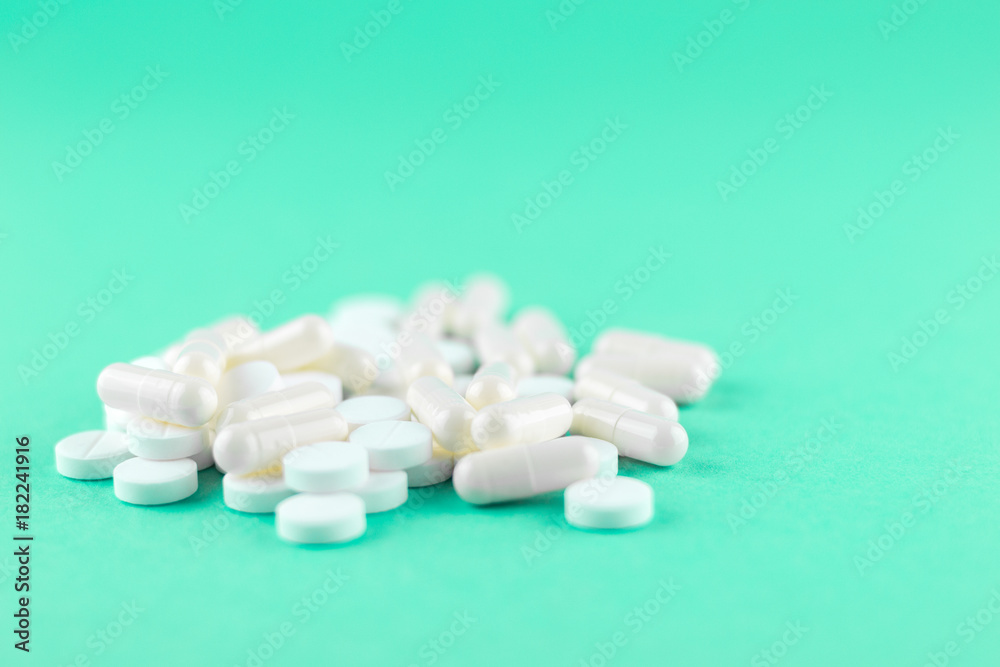 Close up white pills and capsules on aquamarine background with copy space. Focus on foreground, soft bokeh. Pharmacy drugstore concept