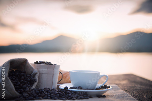 Coffee cup and coffee beans on wooden table in morning sunlight