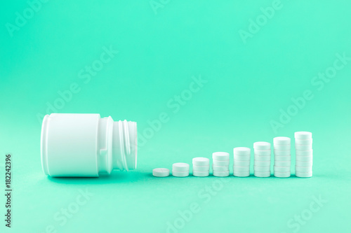 Close up pyramid concept of white pills and bottle on aquamarine background with copy space. Focus on foreground, soft bokeh. Pharmacy drugstore concept