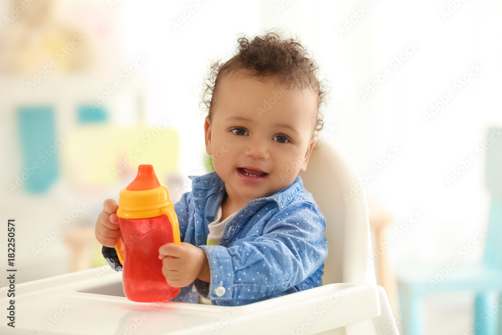 Cute little baby with bottle of water sitting on chair in room Cute little baby with bottle of water sitting on chair in room