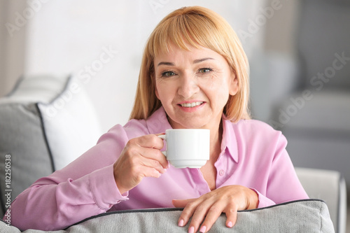 Beautiful mature woman drinking coffee while sitting on sofa at home