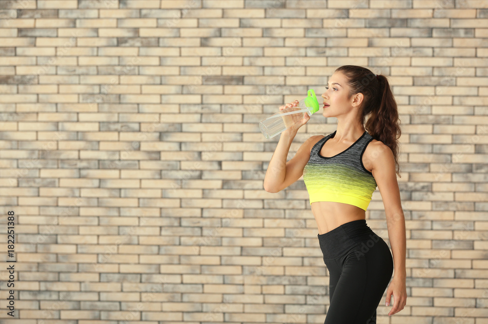 Sporty young woman with bottle of water against brick wall Sporty young woman with bottle of water against brick wall