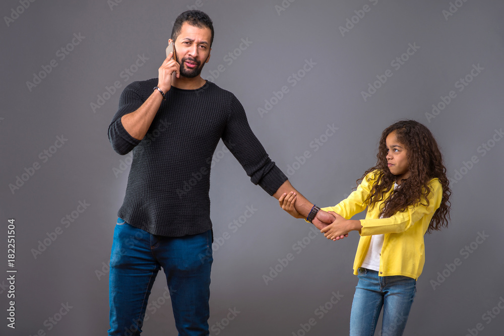 Obraz premium Black father talking on his phone while his daughter pulling his
