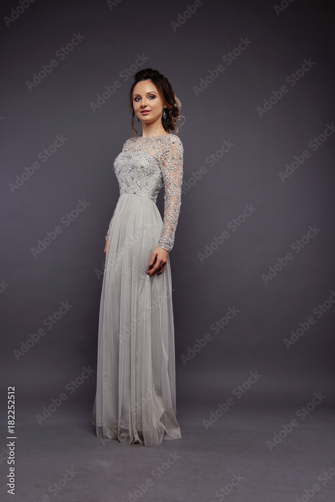 Studio Portrait of a Beautiful Bride Model in a Light Gray Wedding Dress with Elegant  Hairstyle and Pink Lips at Gray Background