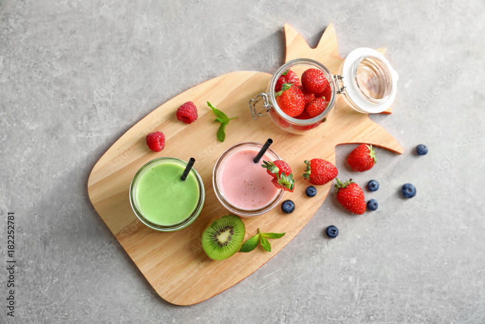 Glass jars with different milkshakes on wooden board