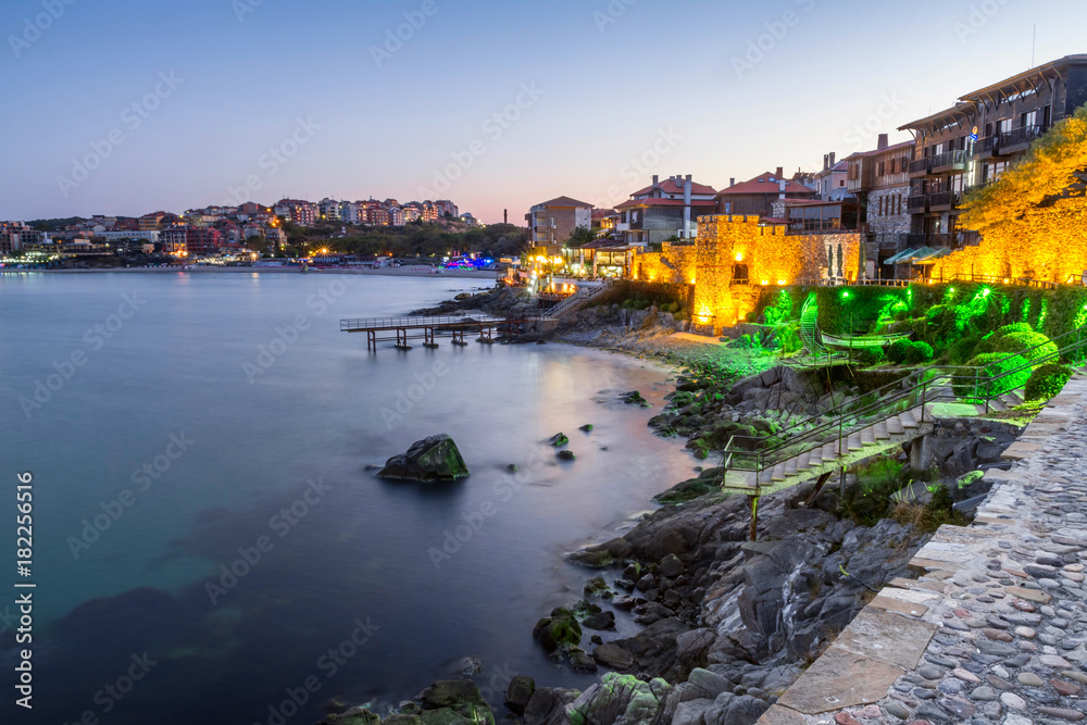 Seaside sunset landscape - embankment with fortress wall and illumination in the city of Sozopol on the Black Sea coast in Bulgaria