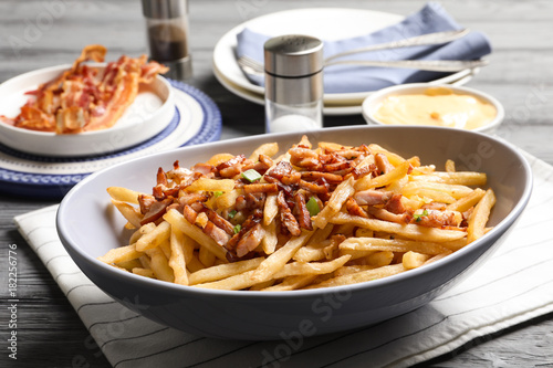 Plate with french fries and bacon on table