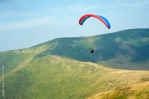 Tandem flies over a mountain valley on a sunny summer day. Paragliding in the Carpathians in the summer. Passenger on the paraglider holds a selfie stick and shoots the video.