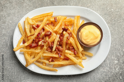 Plate with french fries and bacon on light background