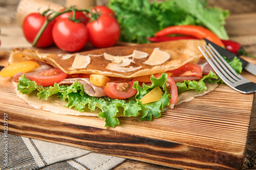 Board with thin buckwheat pancake, bacon and vegetables on table