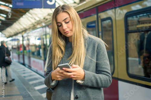 Young woman using mobile phone while waiting for train at railway station.