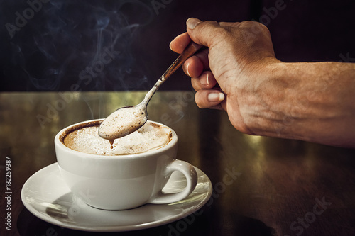 Fotografia A woman holding coffee spoon to stir hot coffee on wooden table