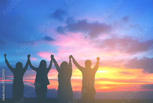 Silhouette of happy business team hold hands up in sunset sky background, business teamwork, business achievement conceptual