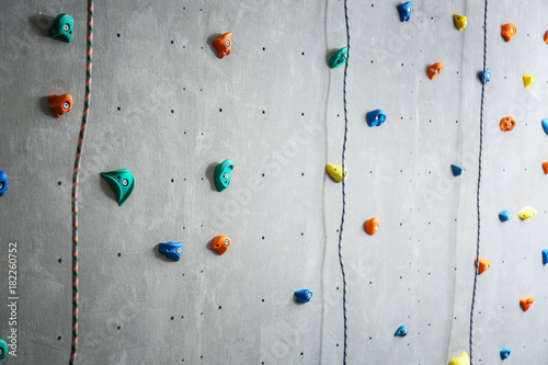 Grey wall with climbing holds and ropes in gym
