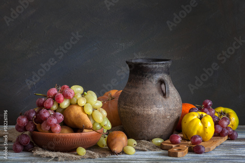 Still life in a rustic style: a set of clay dishes, grapes and pears on a wooden table. Natural light from the windows.