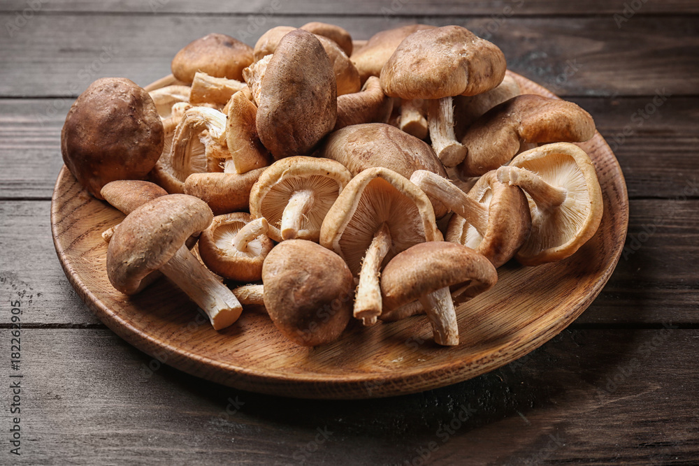 Dish with raw shiitake mushrooms on wooden table Dish with raw shiitake mushrooms on wooden table