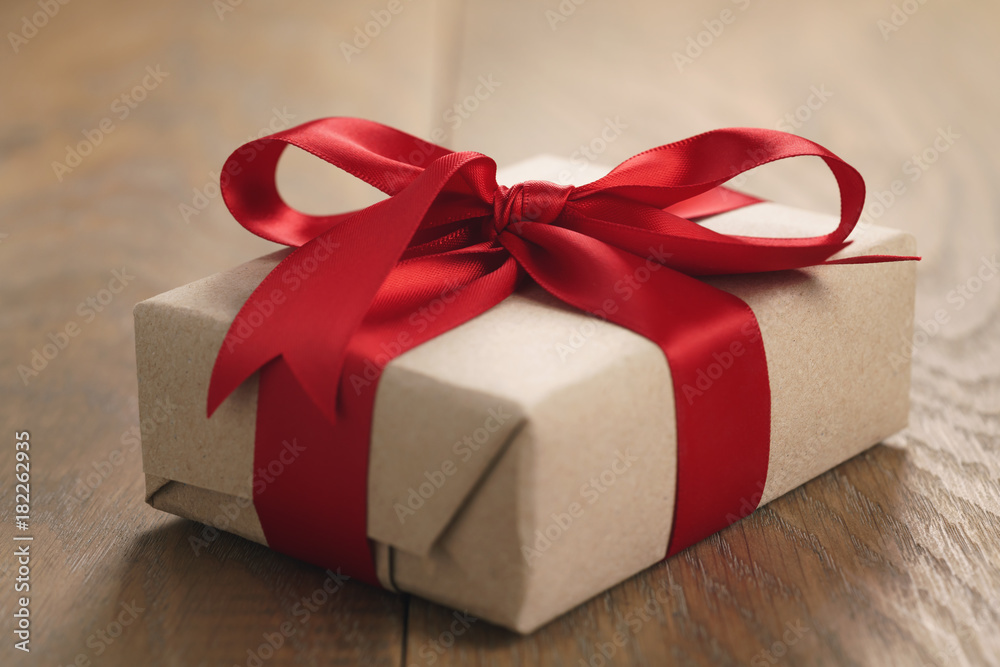 brown paper gift box with red ribbon bow on oak table