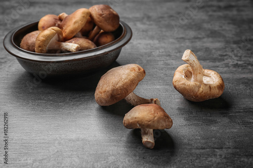 Raw shiitake mushrooms and bowl on wooden table