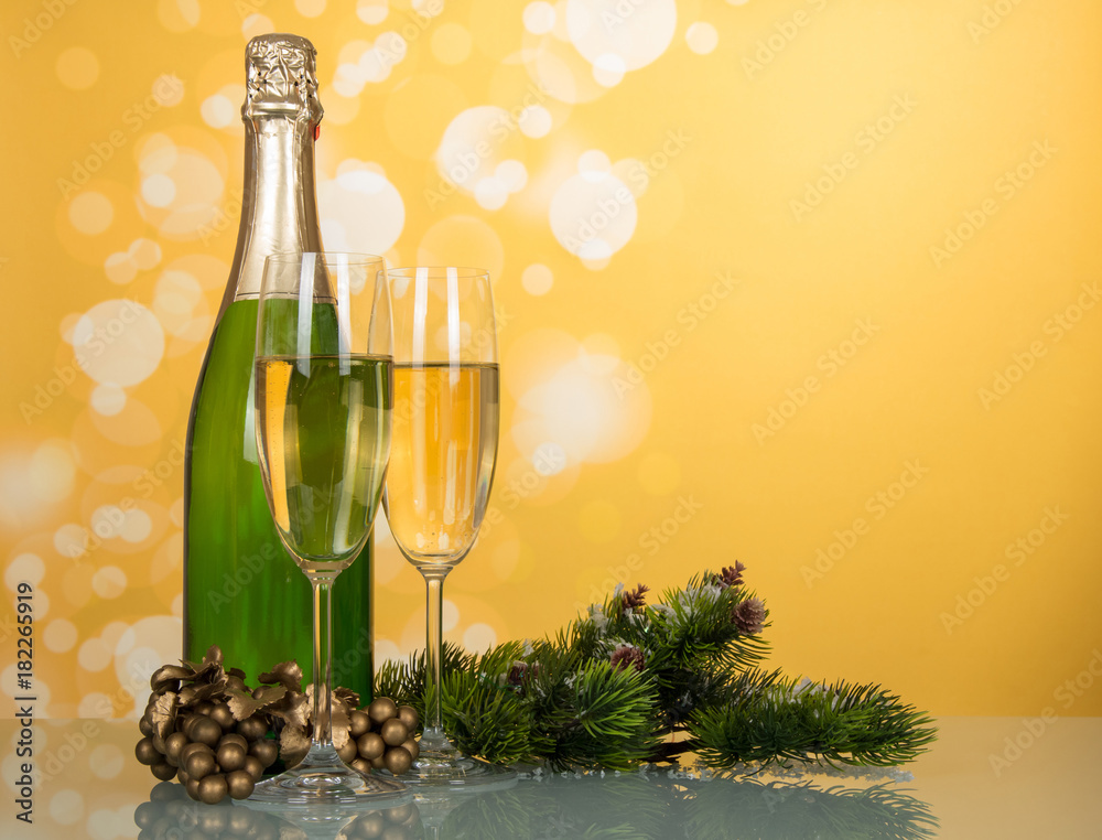 Bottle of champagne, two glasses, decorated pine branches on yellow